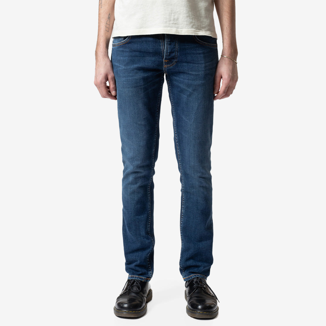 Nudie Jeans Grim Tim slim fit-jeans för herr i Indigo Myth Mid Blue Wash med rak benvidd och kontrasterande slitningar.