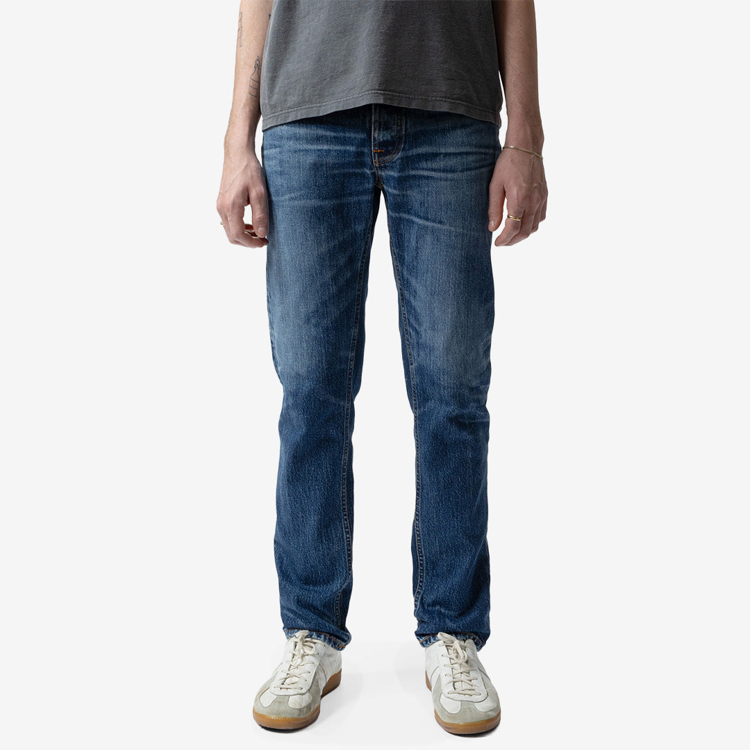 Nudie Jeans Solid Ollie Life Tracks slim fit-jeans för herr i Mid Blue Wash med autentiska slitningar och smal benvidd.