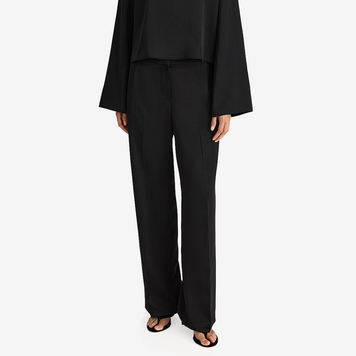 Stylein Maggie Trouser Black, svarta hellånga byxor i stretchig satin med pressveck och snedställda sidfickor.